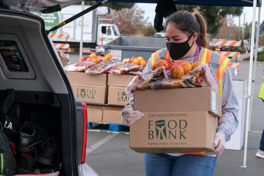 A woman volunteers at a food bank, loading boxes of fruits and other items into the back of a van.